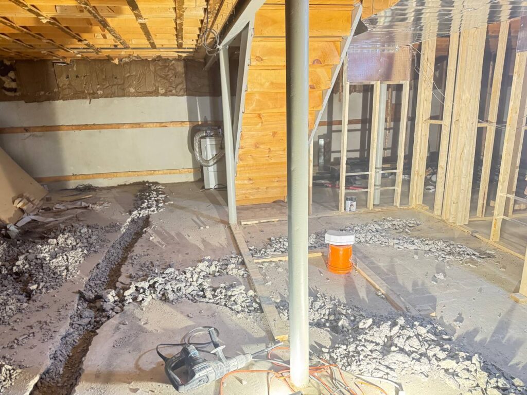 Excavated trench showing new PVC building drain pipe replacing old clay pipe in Toronto basement