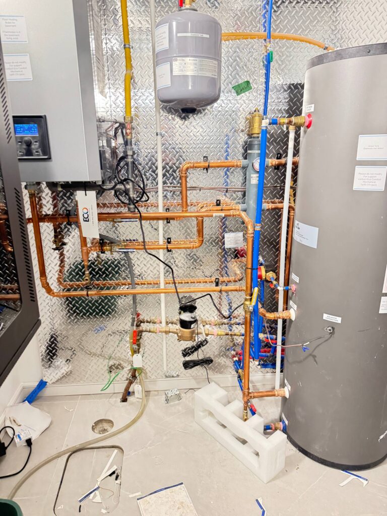 Professional installation of a high-efficiency water heater and complex copper hot and cold water piping system in a mechanical room.