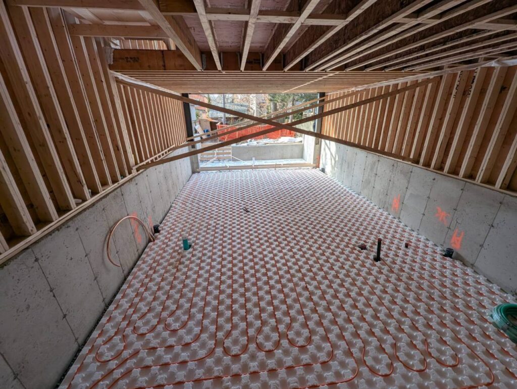 Professional plumbers installing radiant floor heating and furnace room piping in new custom residential home Toronto