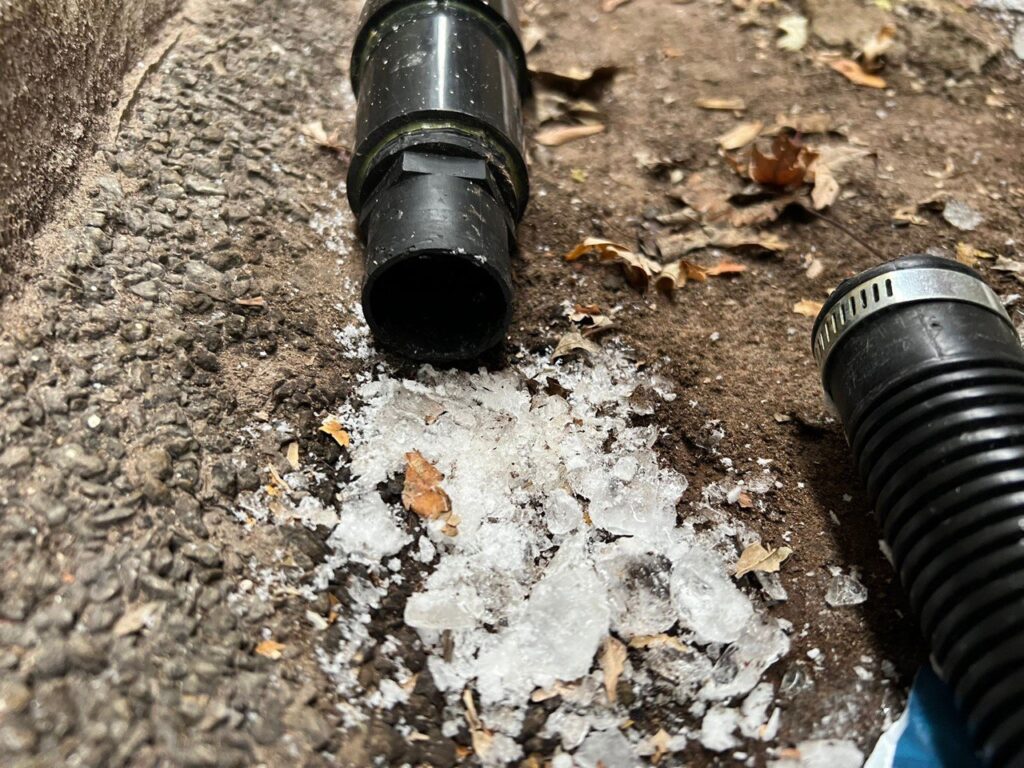 A properly sloped PVC sump pump discharge pipe exiting a house to prevent freezing.