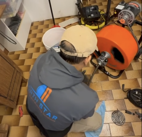 North Star Solution technician using a professional drain snaking machine to clear a clogged floor drain in a Toronto home.